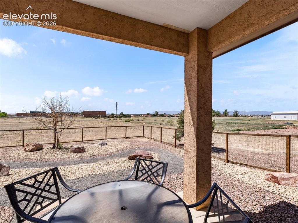 Image 31 of 44: Covered patio with textured stucco columns, concrete flooring, and gravel l