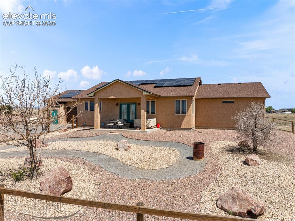 Image 39 of 44: Rear exterior featuring a covered patio, solar panels, and a gravel landsca