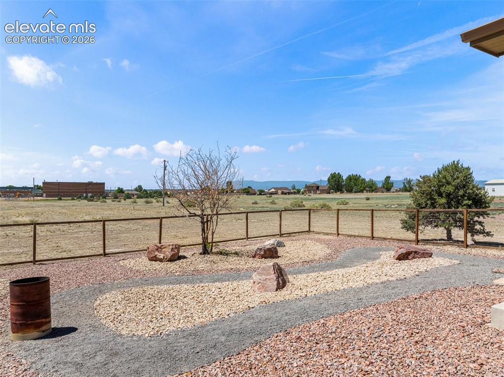 Image 44 of 44: Landscaped yard featuring a gravel pathway, decorative rocks, and a wood fe
