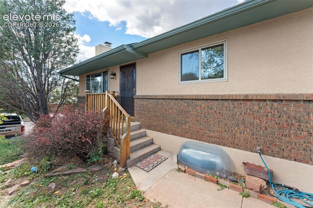 Image 15 of 50: Stucco and brick exterior with a dark entry door, concrete steps, and a woo