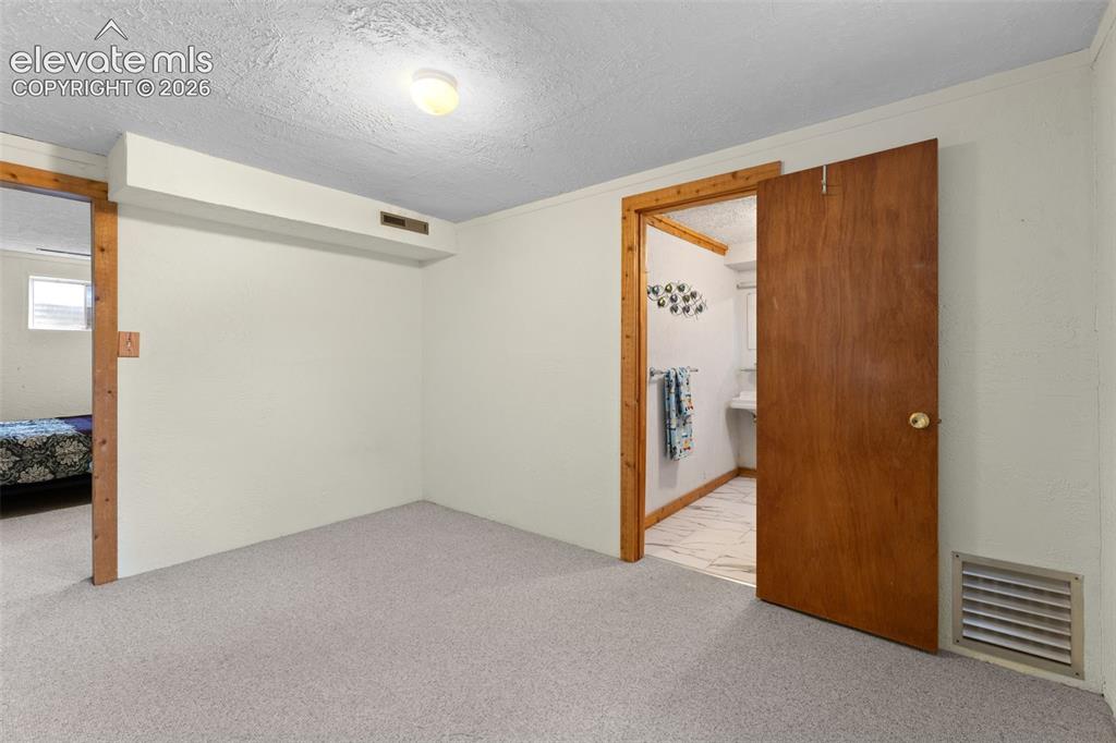 Image 27 of 50: Light-colored carpeted flooring, white painted walls, and wood-trim doorway