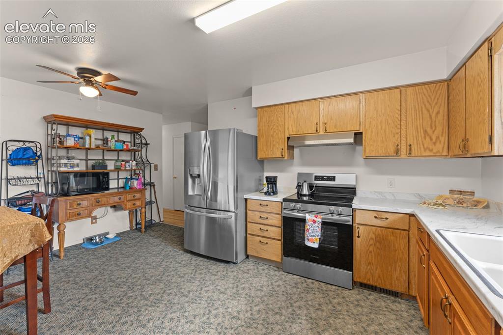 Image 4 of 50: Kitchen featuring wood cabinetry, stainless steel appliances, and white cou