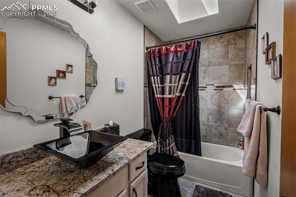 Image 29 of 50: Bathroom featuring a vessel sink with a black faucet, quartz countertop, ti