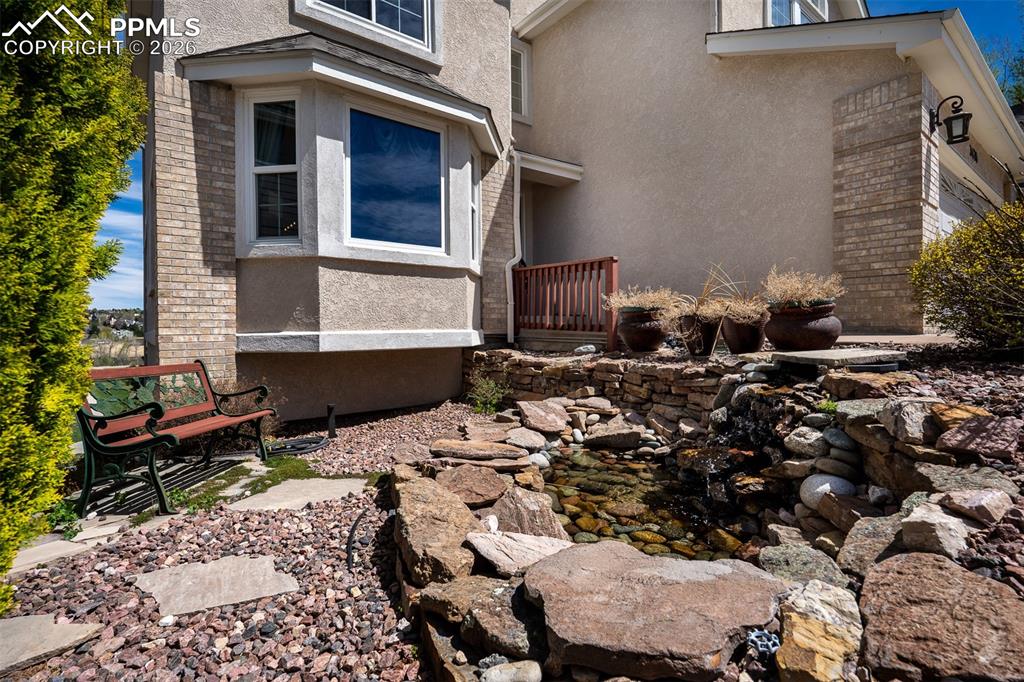 Image 3 of 50: Bay window, stucco and brick facade with a rock garden and a tiered rock wa