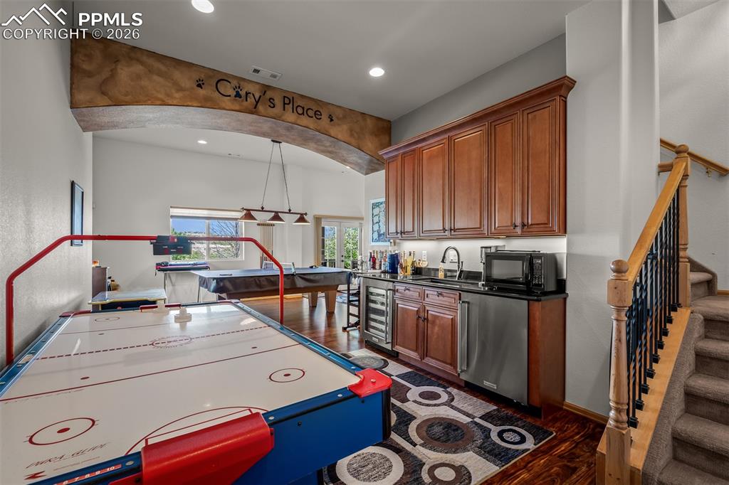 Image 34 of 50: Entertainment room featuring a wet bar with wood cabinetry, dark countertop