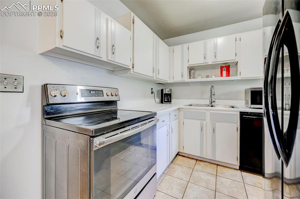 Image 10 of 30: Kitchen featuring black appliances, open shelves, light countertops, white