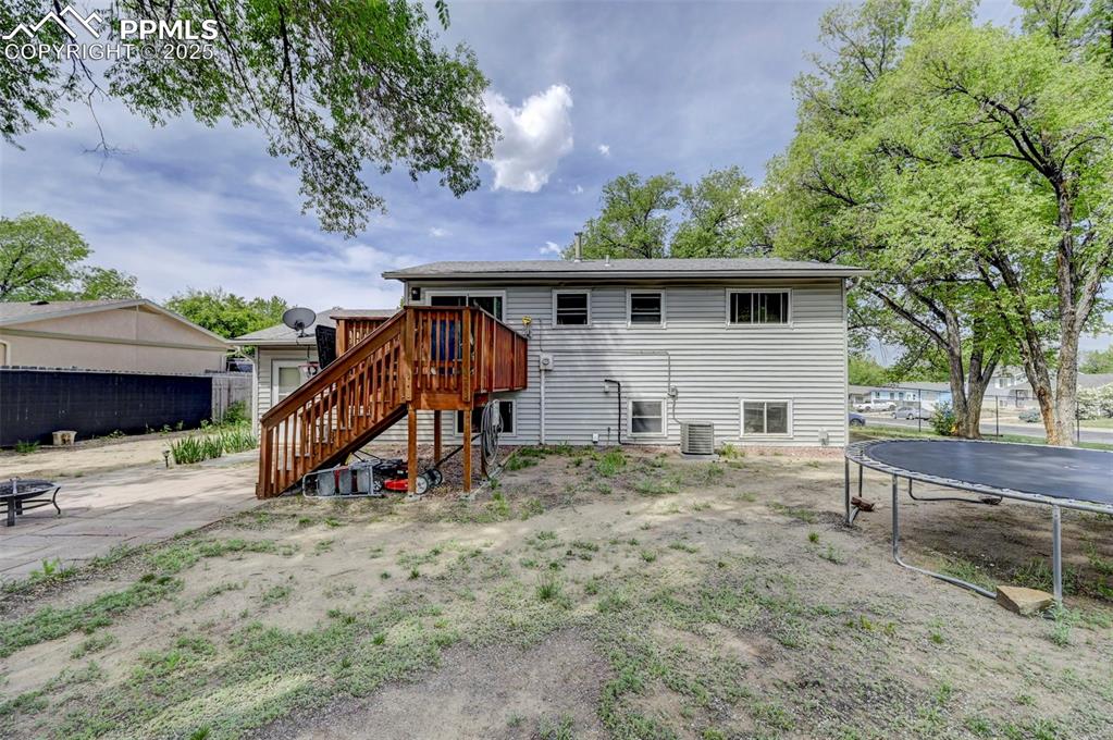 Image 28 of 30: Rear view of house featuring a trampoline, stairway, and a wooden deck