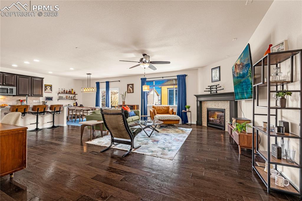 Image 5 of 37: Living area with dark wood-style floors, a ceiling fan, a tiled fireplace, 