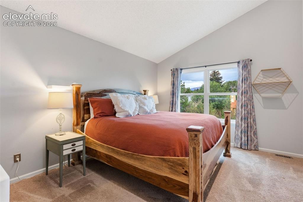Image 16 of 37: Vaulted ceiling, large window, natural wood bed frame, light gray walls, an