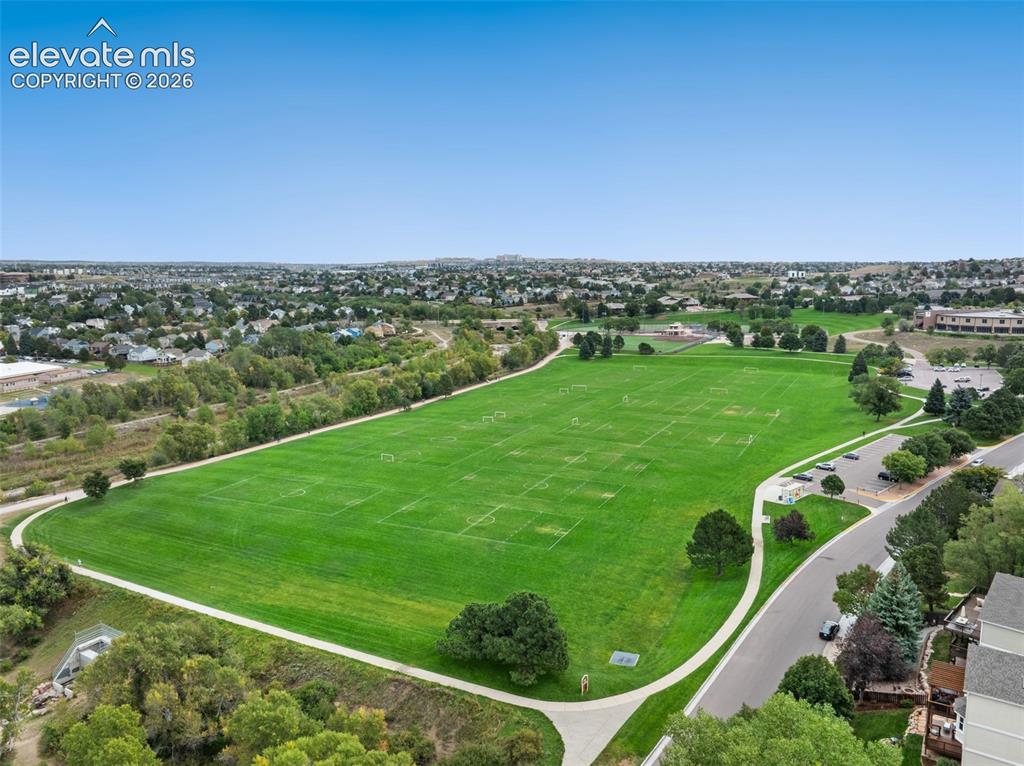 Image 36 of 37: Expansive green fields with delineated sports areas, bordered by a paved pa