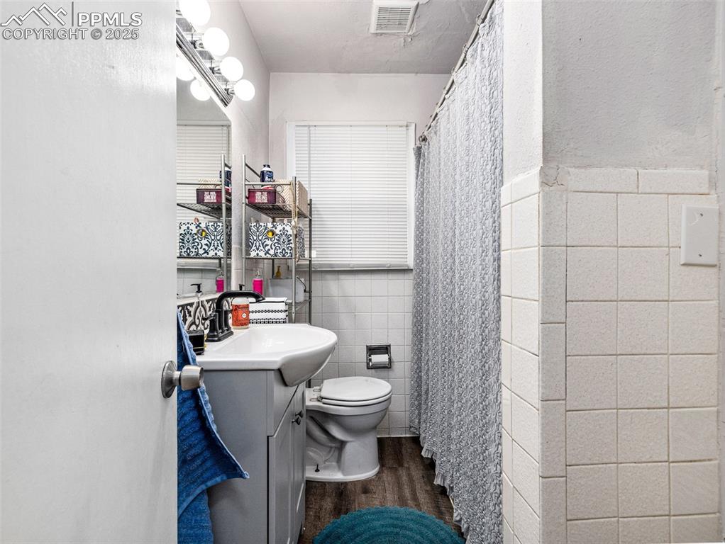 Image 28 of 33: Full bath with tile walls, vanity, a shower with curtain, dark wood-type fl