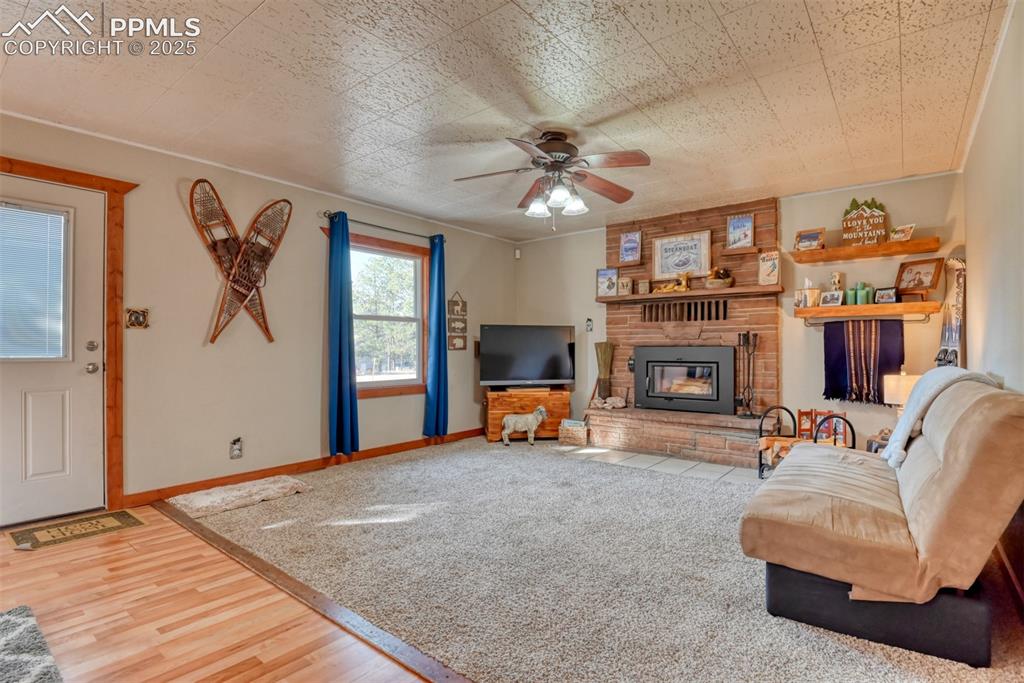 Image 22 of 43: Living area featuring light wood-type flooring, ceiling fan, and a fireplac