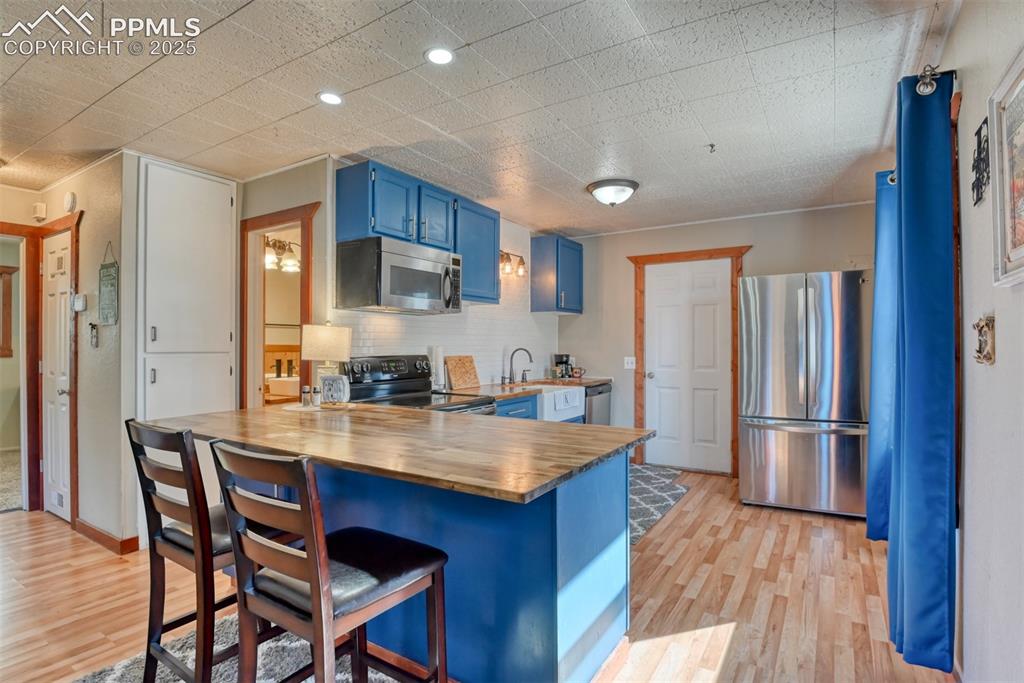 Image 24 of 43: Kitchen with blue cabinets, butcher block countertops, a peninsula, applian