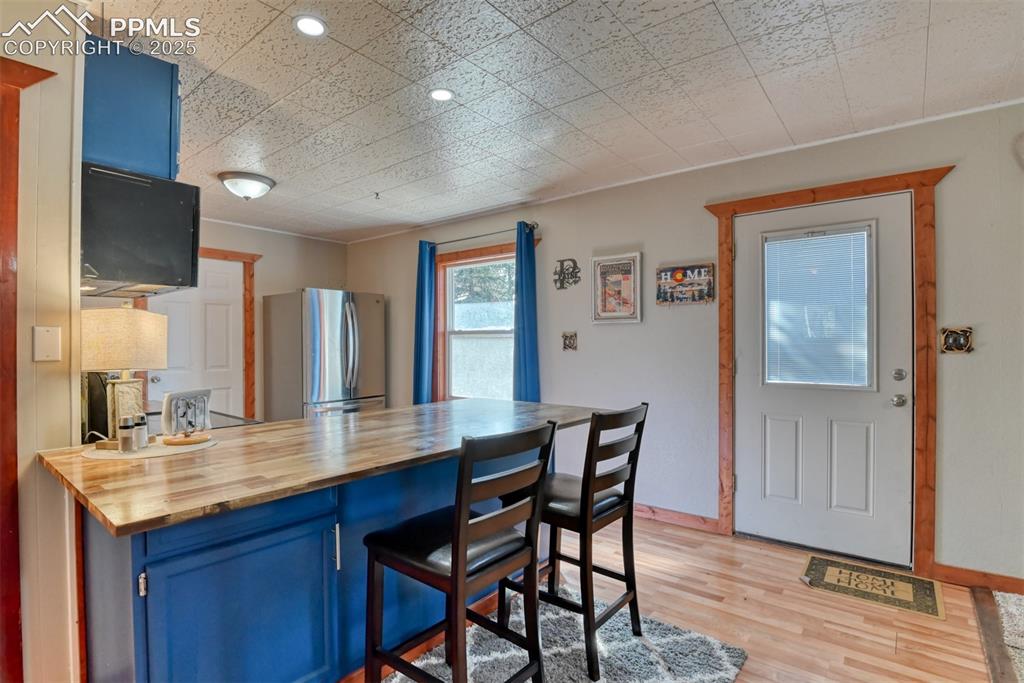 Image 25 of 43: Kitchen with blue cabinets, wood counters, a breakfast bar area, light wood