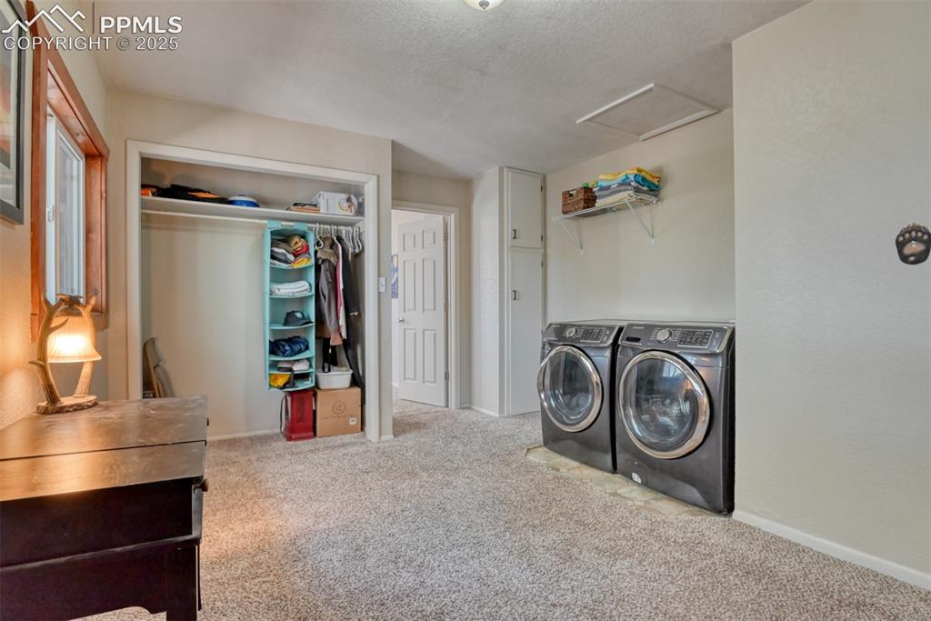 Image 35 of 43: Laundry area featuring light colored carpet, washer and clothes dryer, atti