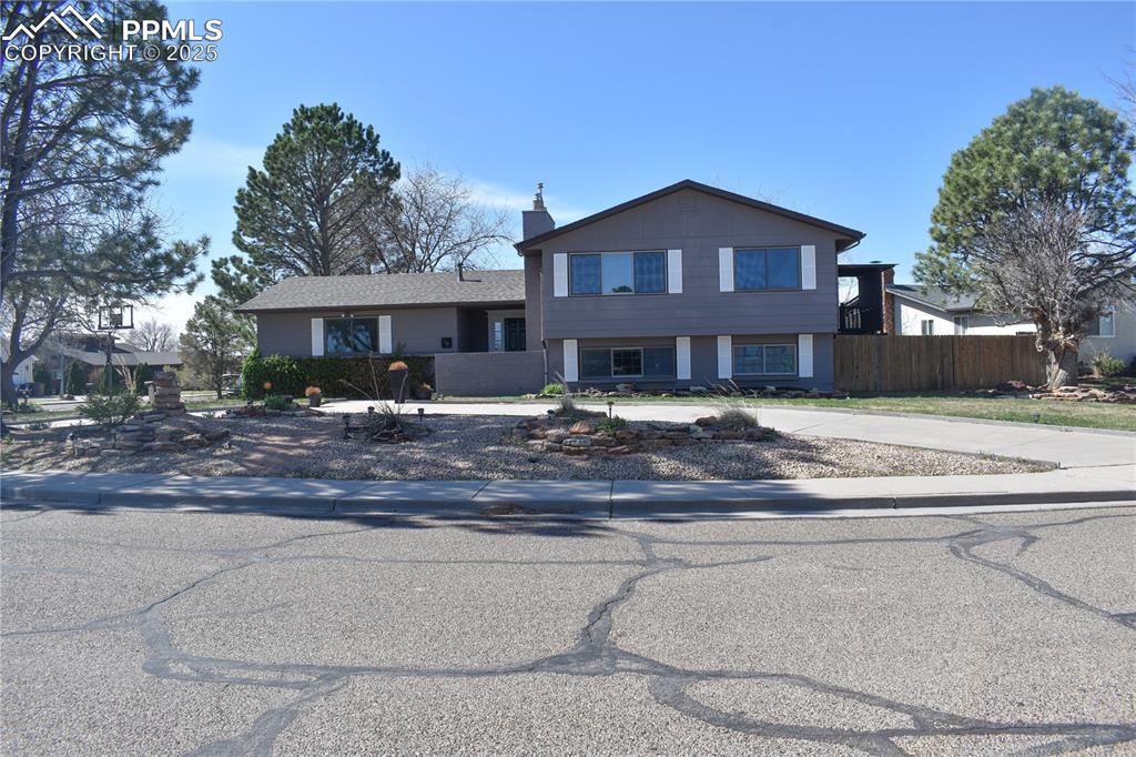 Caption: Tri-level home with a chimney, fence, and curved driveway