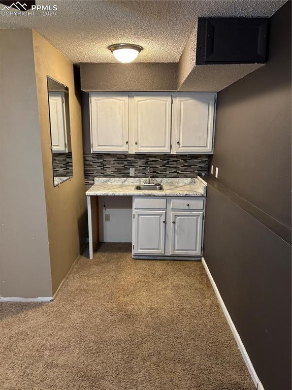 Image 19 of 24: Kitchen featuring backsplash, light countertops, a sink, and a textured cei