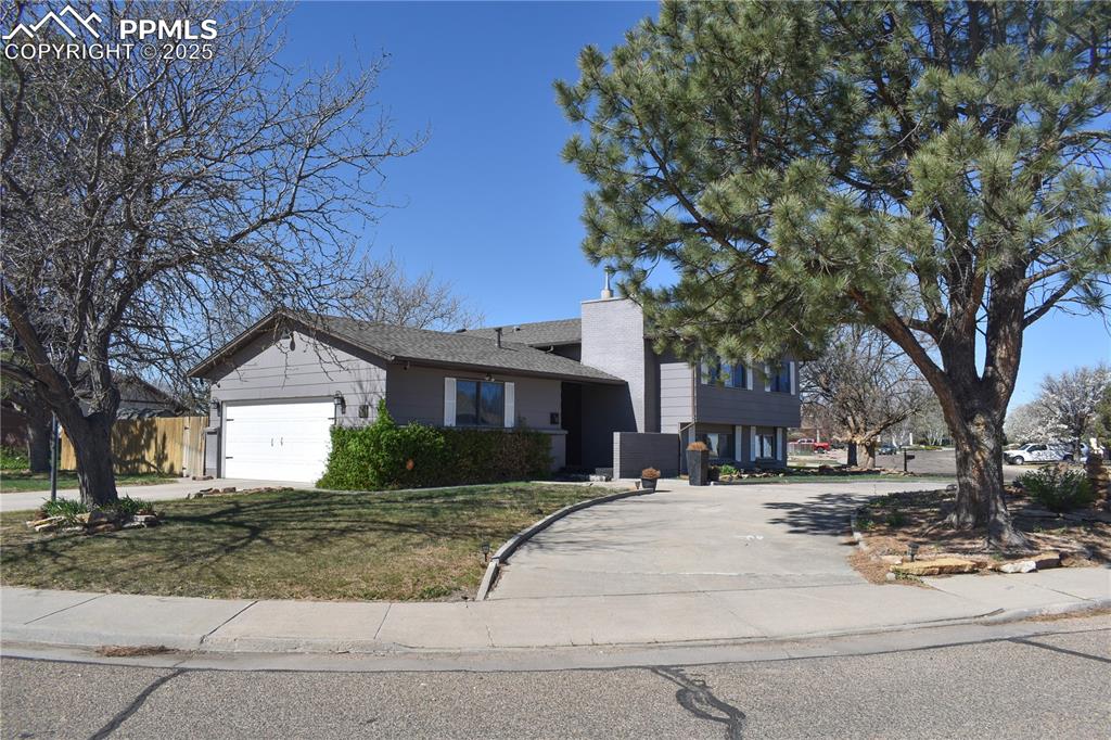 Image 2 of 24: Tri-level home featuring a chimney, a garage, a front lawn, and concrete dr