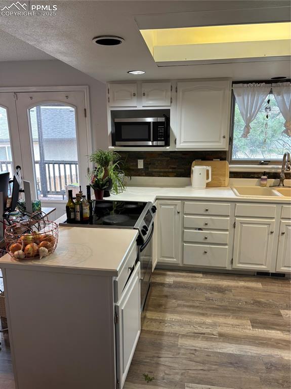 Image 23 of 24: Kitchen with white cabinetry, a sink, stove, and wood finished floors
