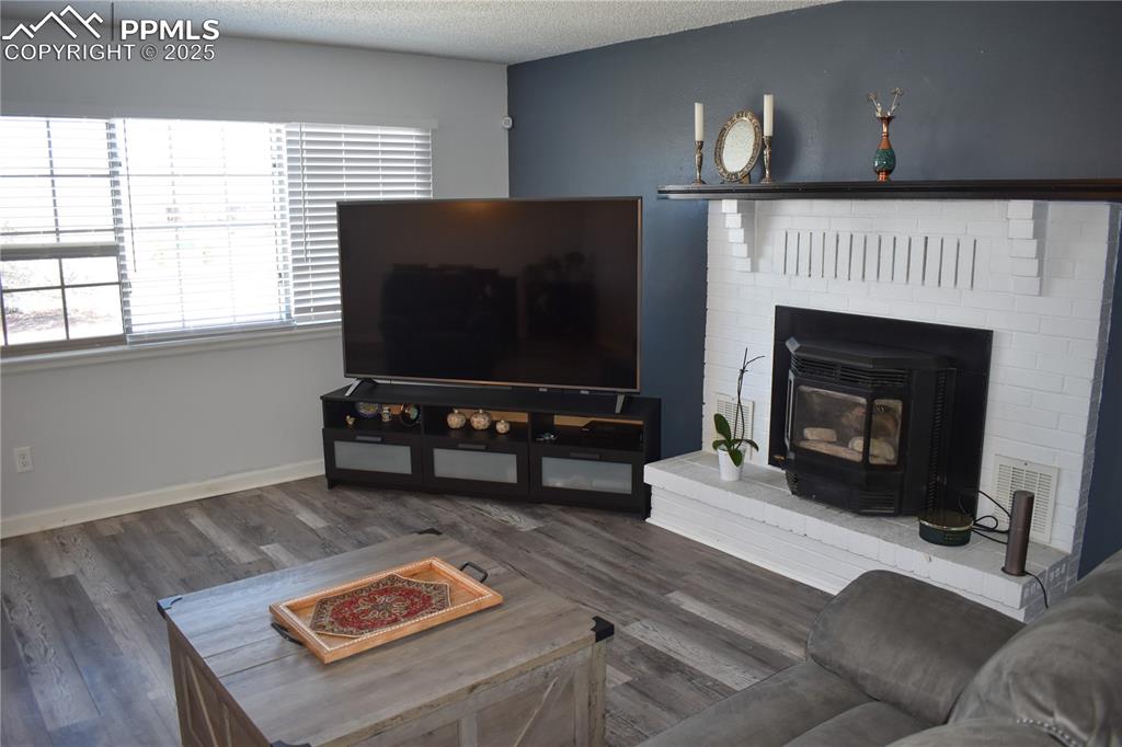 Image 7 of 24: Living area with wood finished floors, a wood stove, a textured ceiling, ba