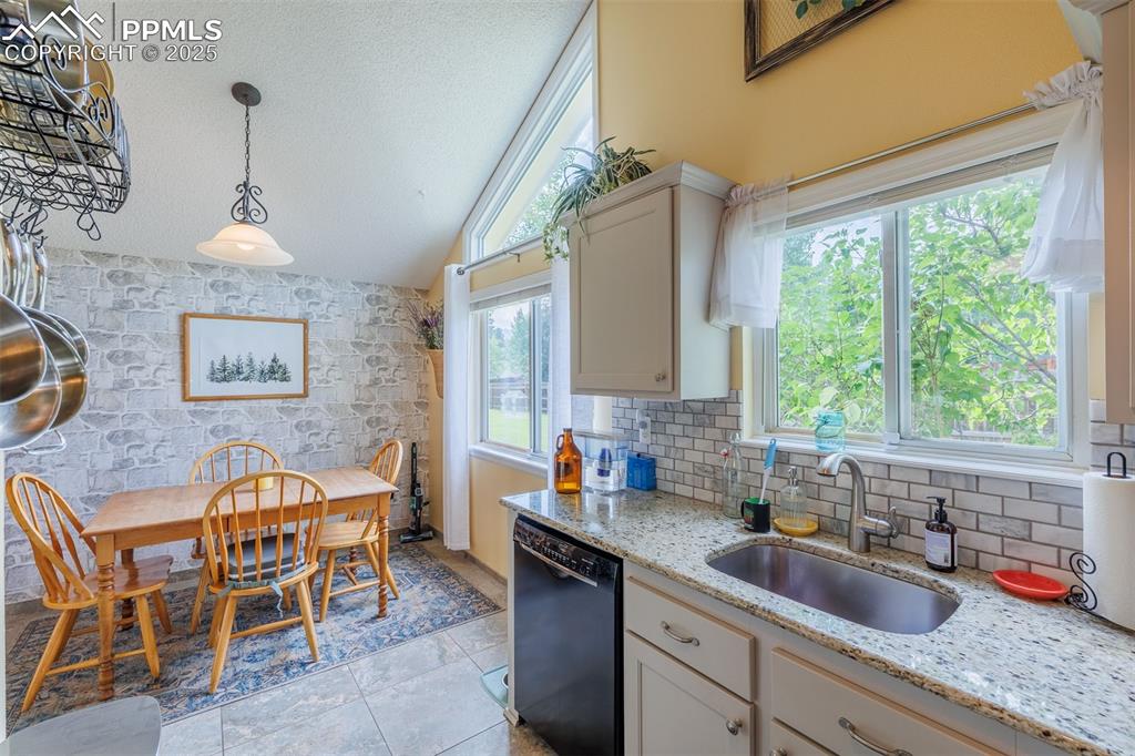 Image 6 of 15: Kitchen featuring vaulted ceiling, hanging light fixtures, and tasteful bac