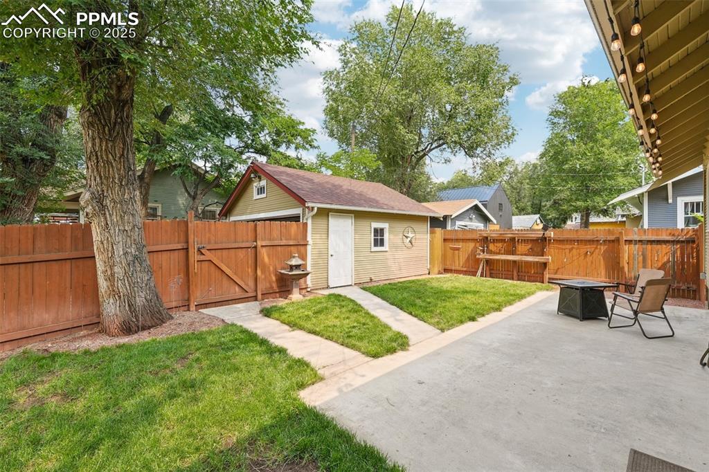 Image 43 of 49: Fenced backyard featuring a fire pit, a patio area, a gate, and an outbuild