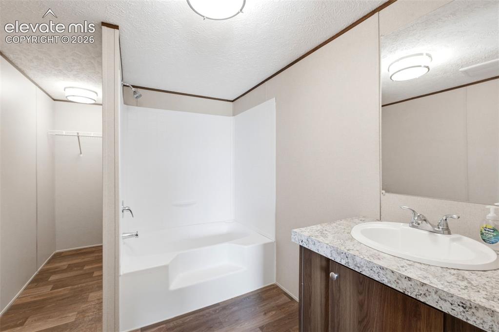 Image 12 of 32: Bathroom featuring a white integrated tub and shower unit, wood-finish floo
