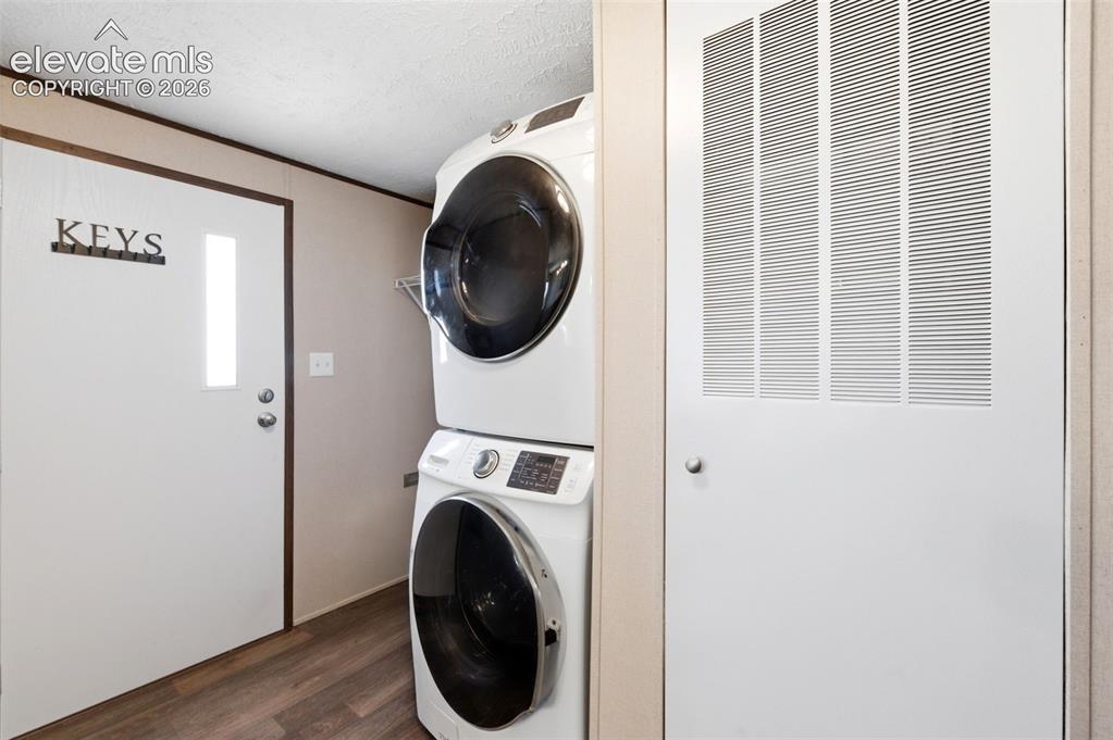 Image 17 of 32: Dedicated laundry area featuring a stacked washer and dryer, wood-finish fl