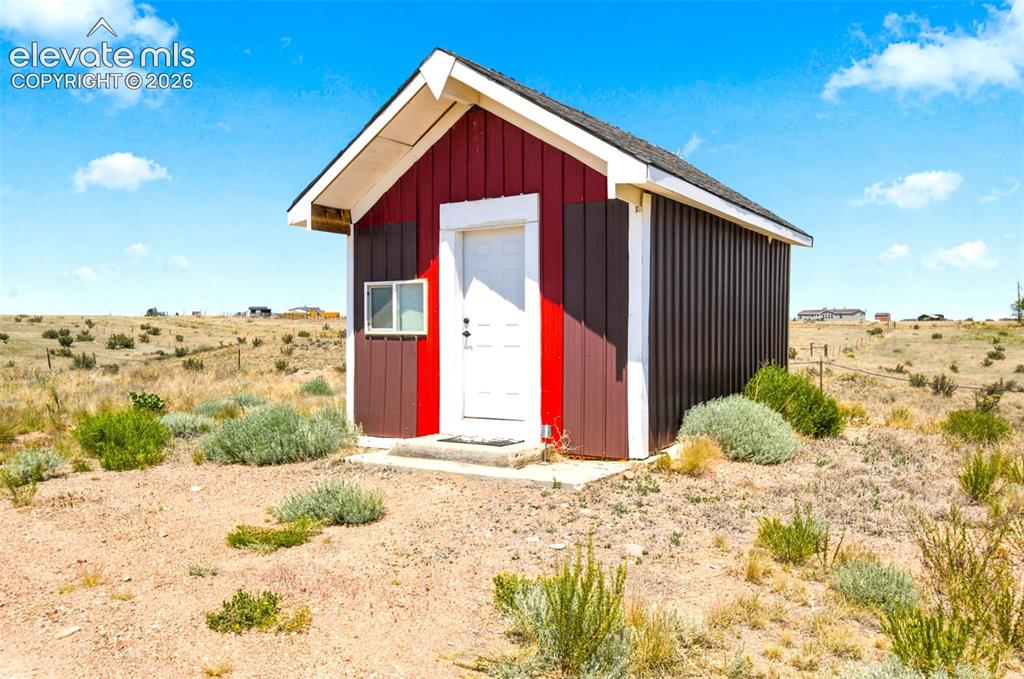 Image 19 of 32: Red and brown vertical siding structure featuring a white entry door and a