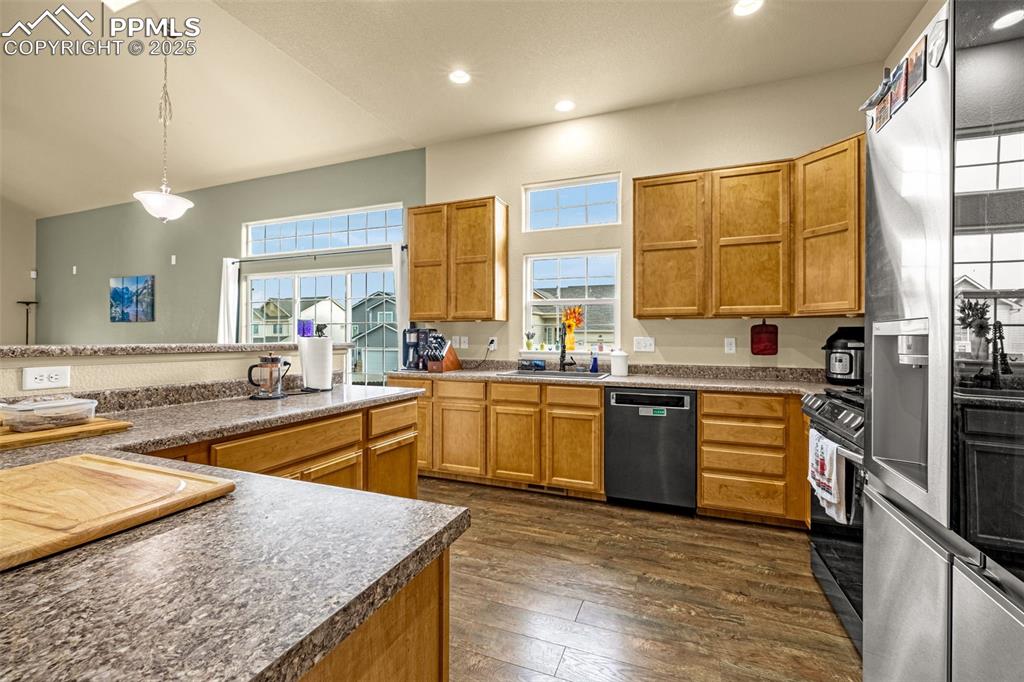 Image 10 of 36: Kitchen with stainless steel appliances, hanging light fixtures, brown cabi