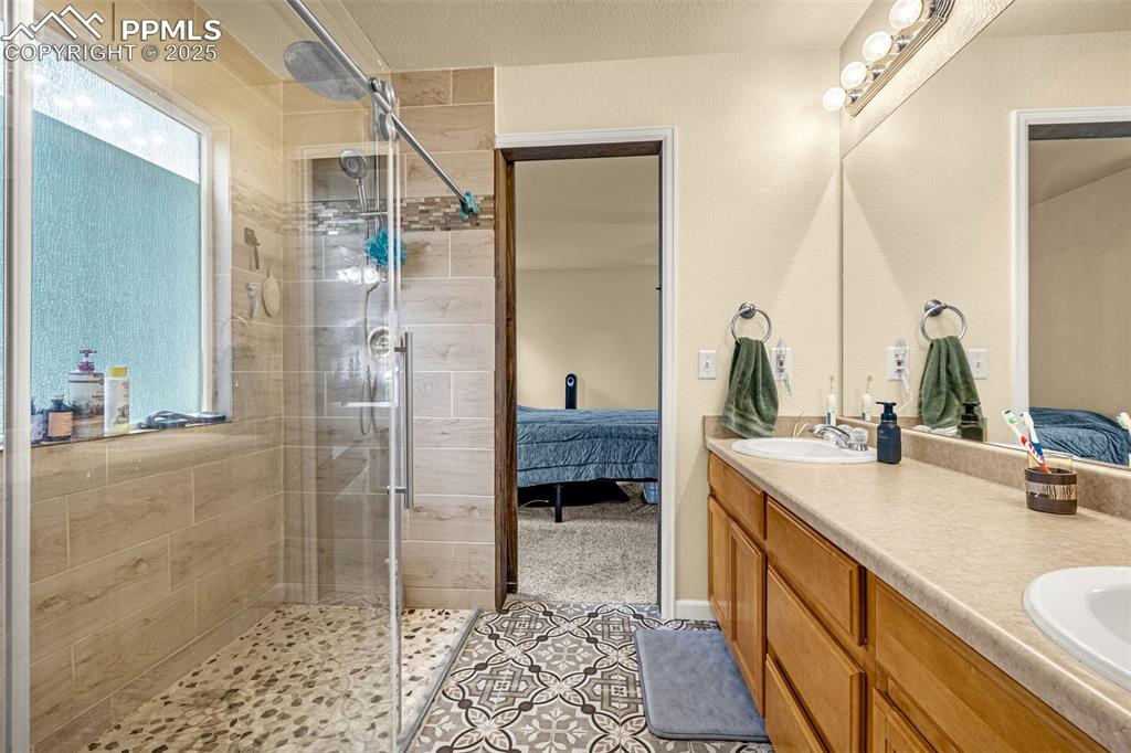 Image 17 of 36: Ensuite bathroom featuring a shower stall, double vanity, and light tile pa
