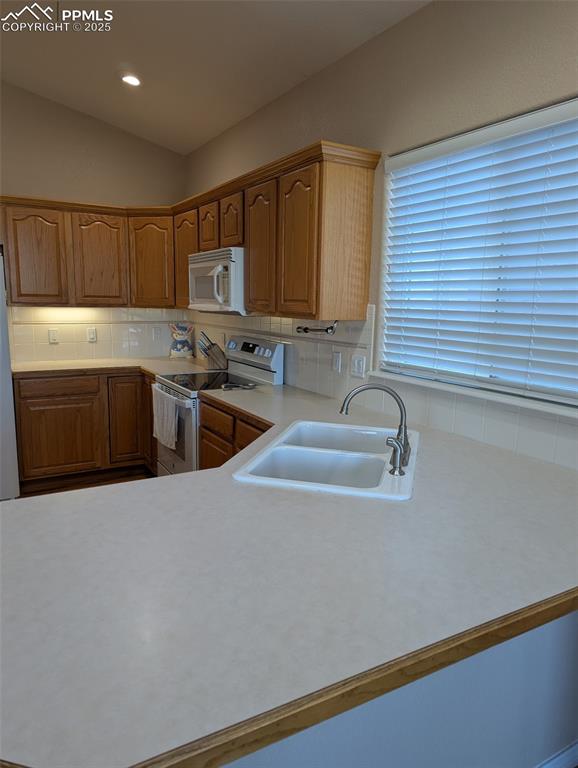Image 10 of 33: Kitchen featuring light countertops, white appliances, backsplash, brown ca