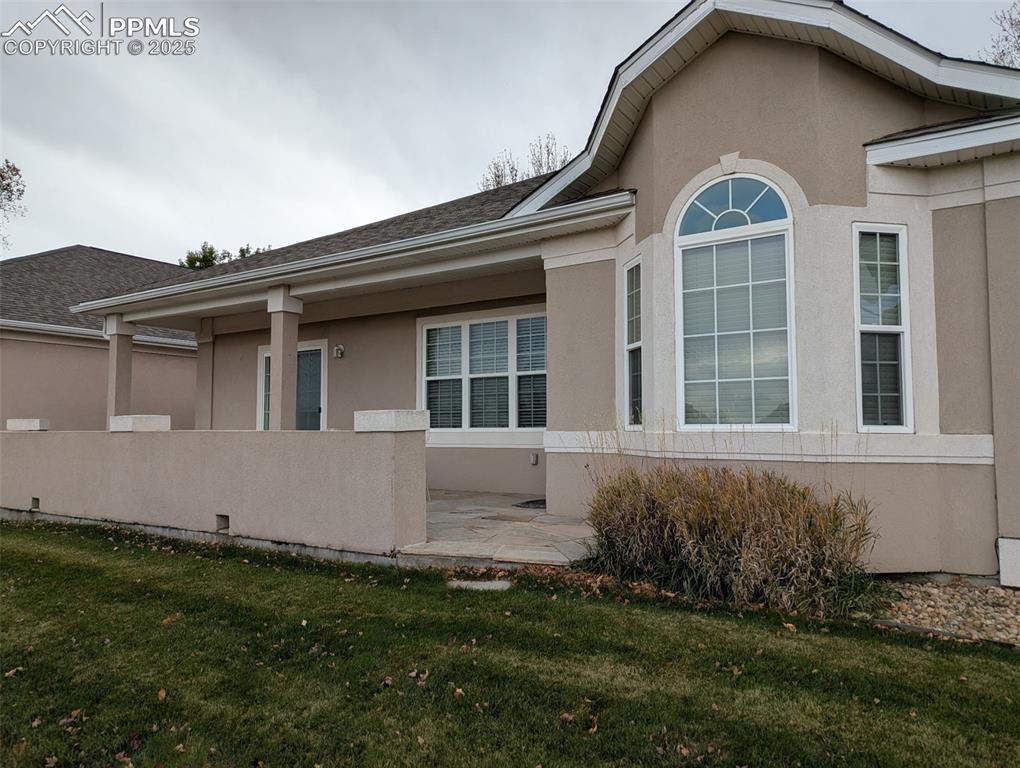 Image 32 of 33: View of side of home with stucco siding, a patio, a lawn, and a shingled ro