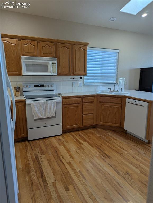 Image 8 of 33: Kitchen with a skylight, white appliances, brown cabinetry, decorative back
