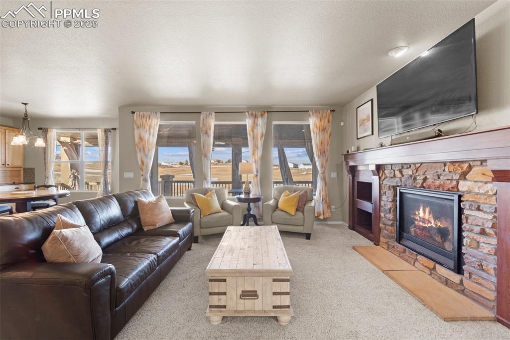 Image 19 of 50: Living room with a fireplace, a chandelier, light carpet, and a textured ce