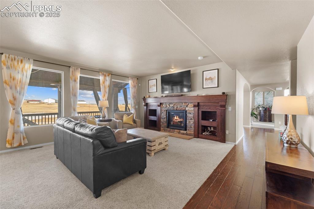 Image 20 of 50: Living room with wood-type flooring, a stone fireplace, and a textured ceil