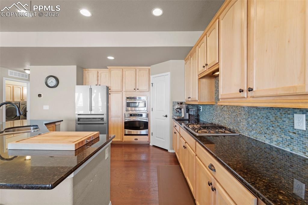 Image 25 of 50: Kitchen featuring light brown cabinetry, sink, dark stone counters, and app