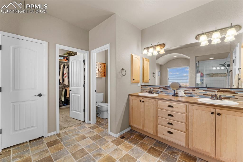 Image 44 of 50: Bathroom featuring vanity, toilet, decorative backsplash, and a shower