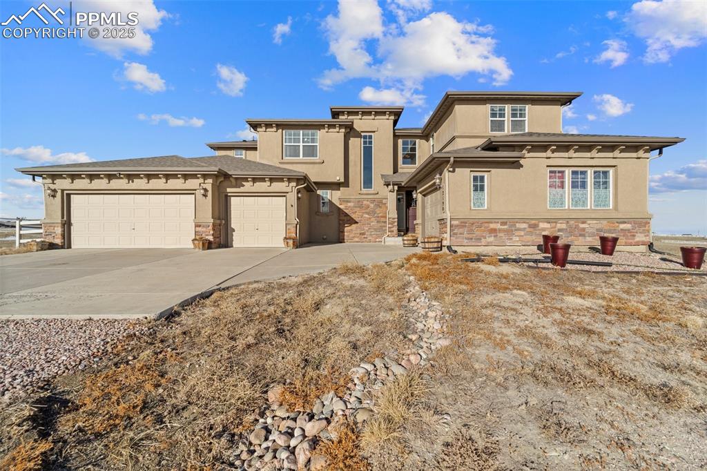 Image 5 of 50: View of front of property with stone siding, stucco siding, a garage, and d
