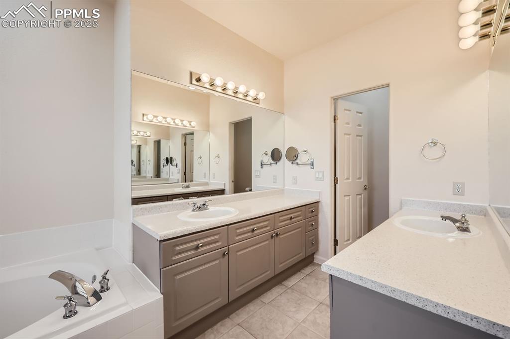 Image 13 of 27: Full bathroom featuring tile patterned floors, a bath, a sink, and two vani