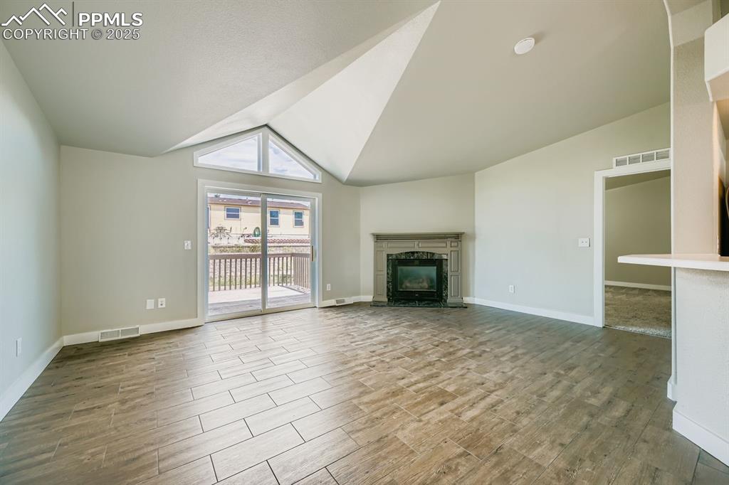 Image 10 of 28: Unfurnished living room with a fireplace, wood tiled floors, and high vault