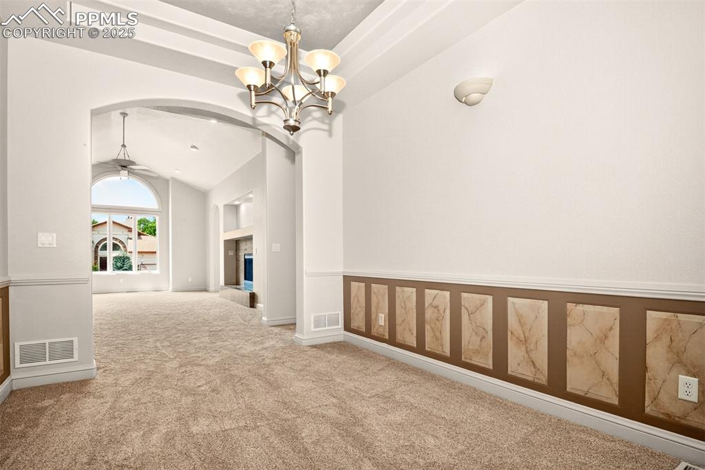 Image 14 of 35: Hallway featuring carpet floors, a chandelier, arched walkways, high vaulte