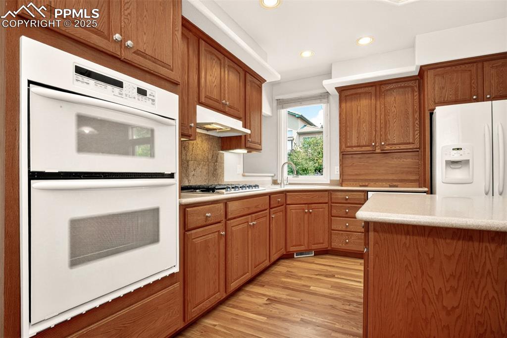 Image 16 of 35: Kitchen featuring white appliances, brown cabinetry, light wood-style floor