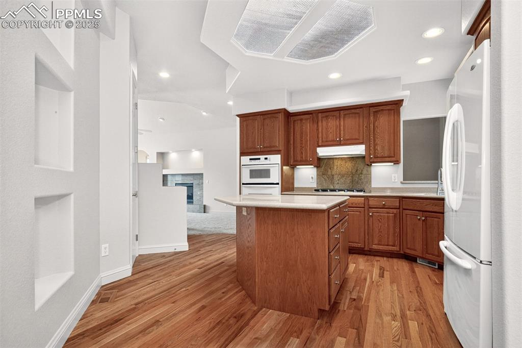 Image 17 of 35: Kitchen featuring a fireplace, light countertops, brown cabinetry, light wo