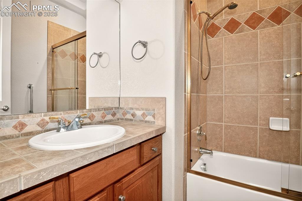 Image 20 of 35: Bathroom with enclosed tub / shower combo, vanity, and backsplash
