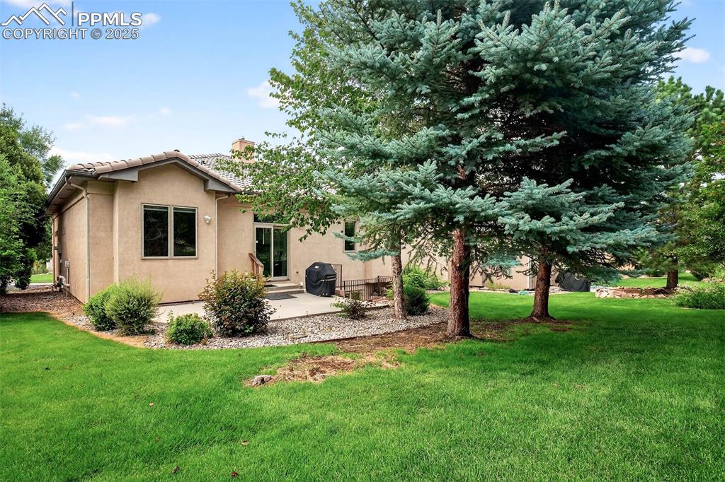 Image 34 of 35: Rear view of property featuring a patio, a lawn, stucco siding, and a chimn