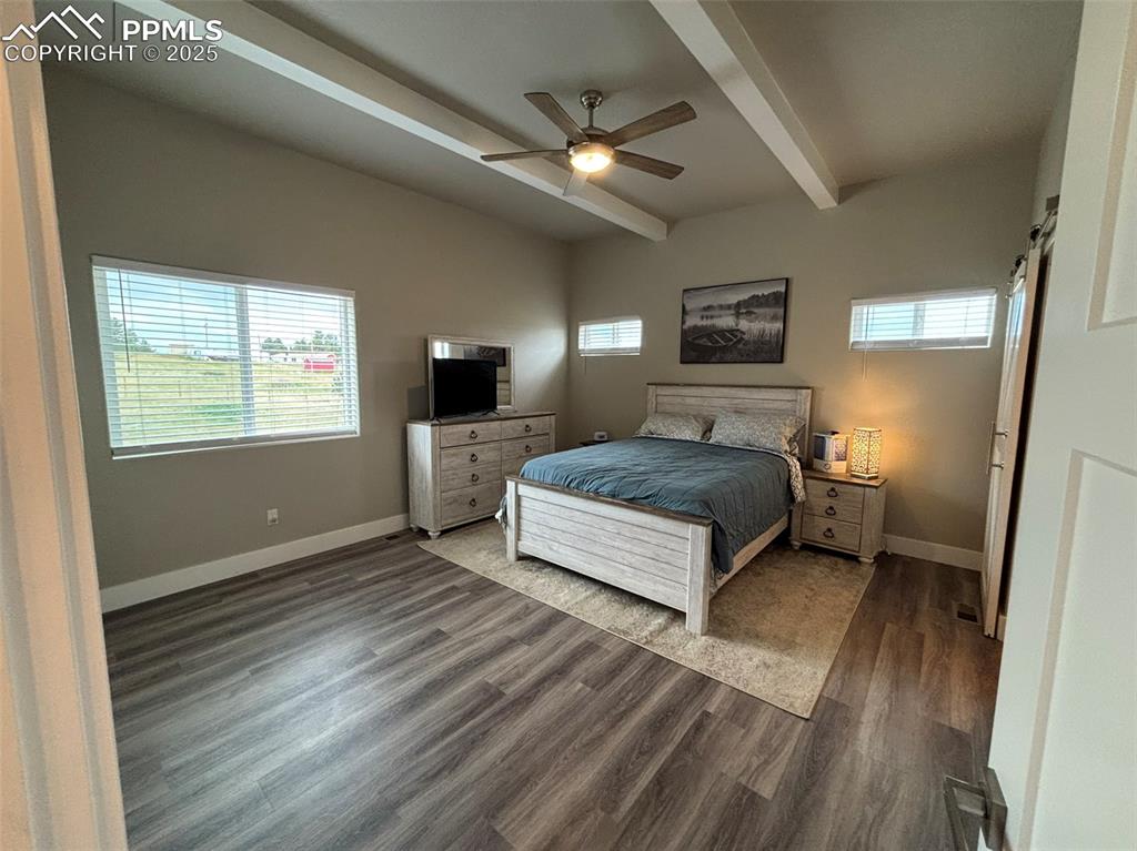 Image 10 of 29: Bedroom featuring a barn door, dark wood-type flooring, beamed ceiling, and