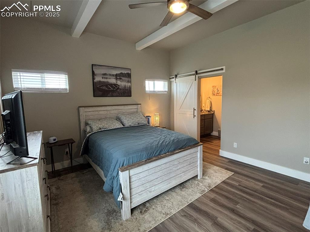 Image 11 of 29: Bedroom with a barn door, dark wood-style flooring, beamed ceiling, a ceili