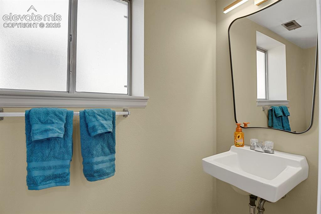 Image 23 of 28: Wall-mounted sink with dual-handle faucet and a framed mirror