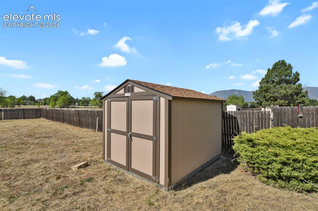 Image 28 of 28: Freestanding shed with double doors and shingled roof, set within a fenced